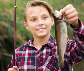 Positive teenage boy holding catch fish in hands