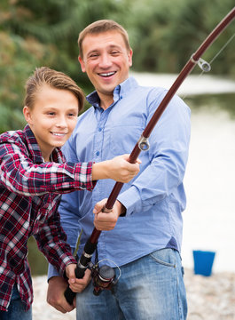 Happy parent and boy fishing together on freshwater lake