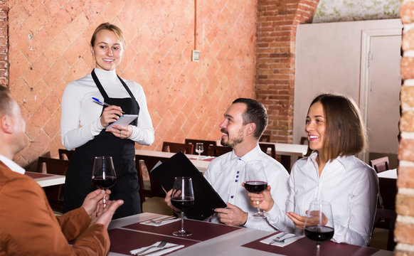 woman waiter receiving order from guests in restaurant