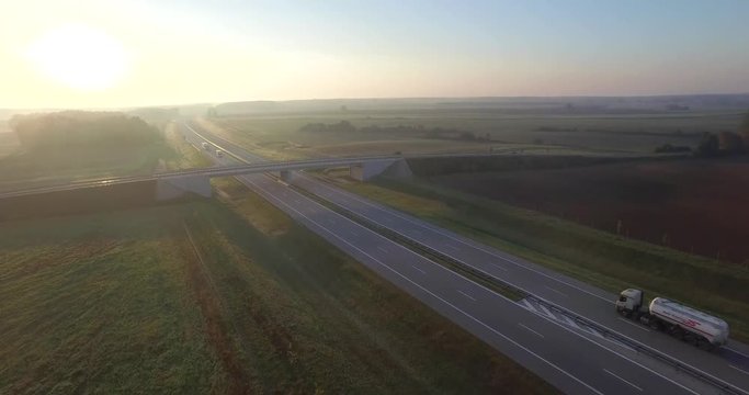 4k pan aerial view of morning landscape with roadway intersection fields traffic transport driving. Flight over highway in countryside bridge local road junction. Transportation logistics cargo
