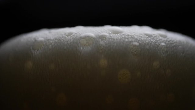 Beer is pouring into glass with foam sliding down side of beer glass