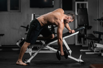 Fototapeta na wymiar Man trains in the gym. Athletic man trains with dumbbells, pumping his biceps