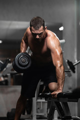 Fototapeta na wymiar Man trains in the gym. Athletic man trains with dumbbells, pumping his biceps