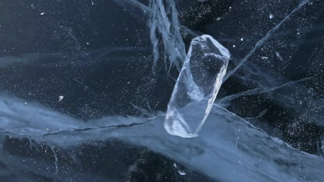 The ice floe rotates on the ice against the background of the amazing mountain landscape. Slow motion. The camera moves behind the ice. A piece of icy is very beautifully spinning on ice with magical