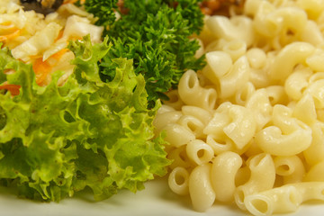 Boiled macaroni on a white plate with fresh herbs.