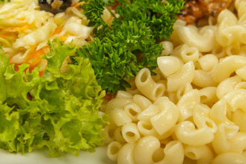 Boiled macaroni on a white plate with fresh herbs.