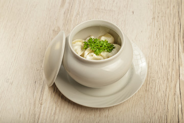 Dumplings in a white pot with sour cream and greens on a wooden background.