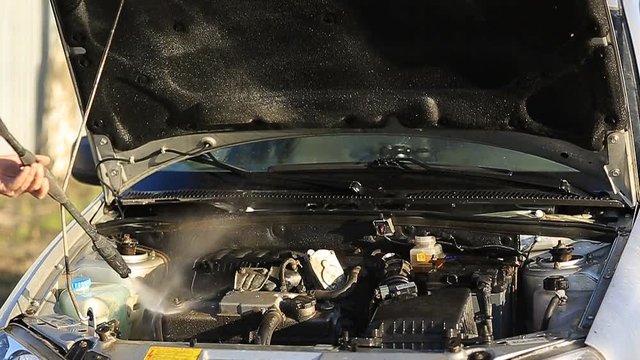 Young attractive man perfusing with water his silver car