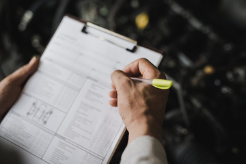 Hand of young man mechanic holding clipboard checklist the car at service center repair