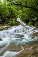 Big cascade streaming over mossy rock in green forest in long exposure