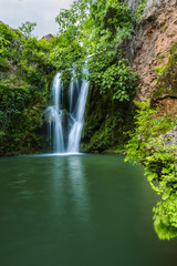 View to tall cascade falling to pond in green forest in long exposure