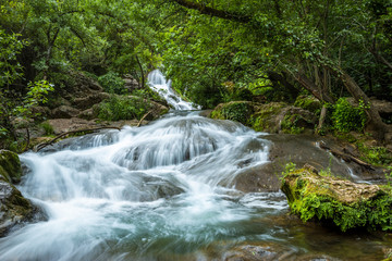Big cascade streaming over mossy rock in green forest in long exposure