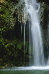 Fototapeta na wymiar Clean cascade water flowing on rock to pond in green woods in long exposure