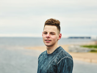 Portrait of young athlete in sportswear looking at camera while recovering from training by sea on...