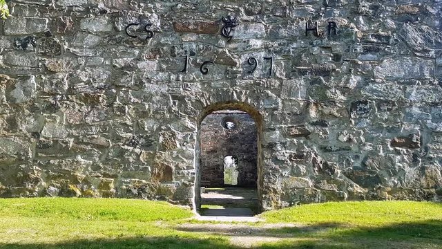 Old church ruin Nes Kirkeruiner entrance glide from grass up to markings above door on a summer day