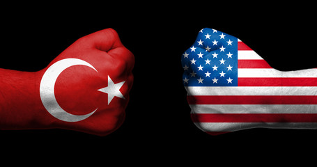 Flags of Turkey and United States painted on two clenched fists facing each other on black...