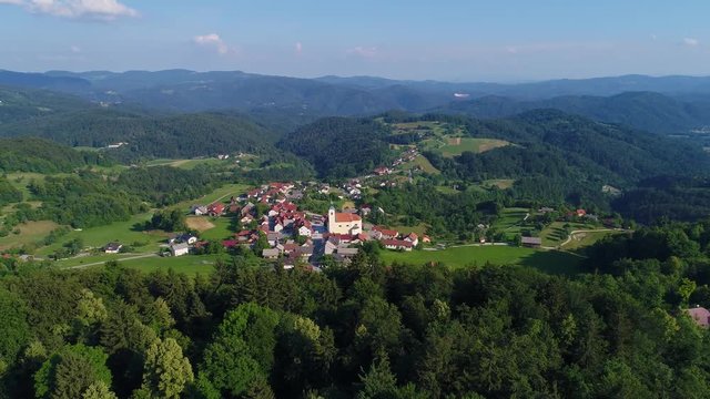 4k aerial shot of a small European town between green hills in a rural area