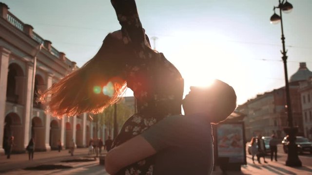 Young couple, male and female, dancing at sunset street, they turning and rotating. Orange lightflares from lenses. Smiling, laughing, happiness, openness. Do not feel shy before passers-by. Super