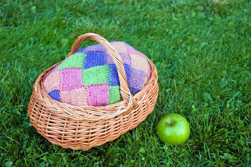 Colorful pink, green, blue, orange, knitted wool cardigan in wooden basket with green fresh apple...