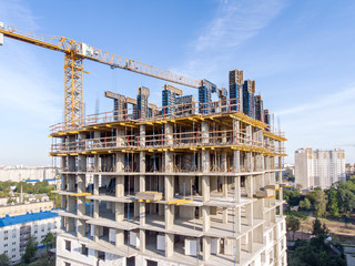 new apartment building under construction and tower crane against blue sky background. drone photo.