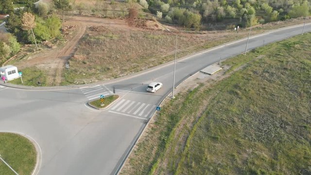 Aerial tracking shot of a white hatchback car on a sunny afternoon