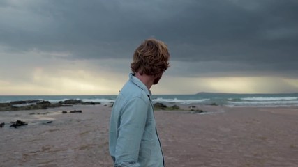 A tight shot of a man looking out to the ocean on a stormy day, and then looking down and laughing. - Powered by Adobe