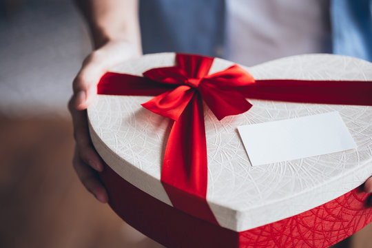 Close up of man hands giving a decorative present giftbox with empty white card - with copy space to insert text.