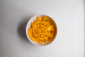 top view of sliced yellow bell pepper in white bowl on white counter top