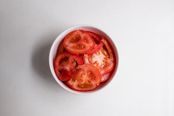 top view of sliced tomatoes in white bowl on white counter top