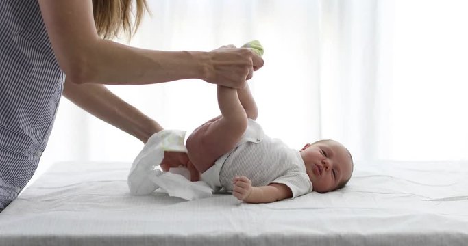 Unrecognizable mother putting on clean diaper on infant while taking care of baby in light room