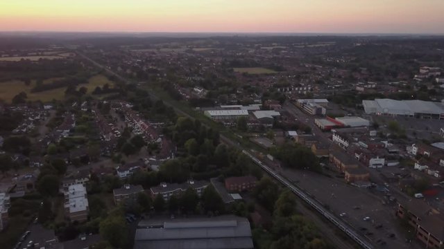 Drone panning up following train go through Borehamwood North London UK rural town during sunset golden hour