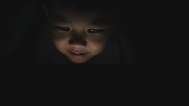 Asian little boy playing tablet or smartphone on a bed in the night