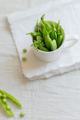 Green peas in a white mug on a white linen napkin