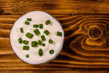 Glass bowl with sour cream and chopped green onion on wooden table. Top view