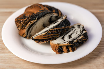 Sweet roll with poppy seeds, sliced sweet poppy seed cake on a plate, on a table