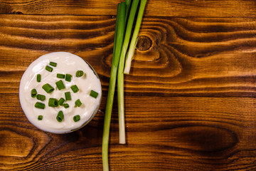 Glass bowl with sour cream and green onion on wooden table. Top view