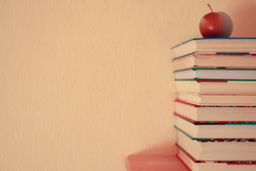 Stack of colorful children books and red apple on bookshelf on yellow wall background with copy...