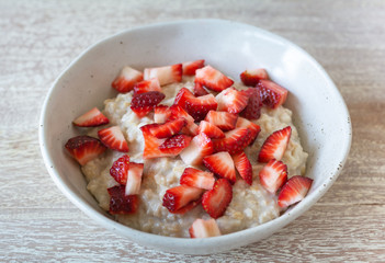 Side view of rolled  organic porridge with cut strawberries in marble bowl on wooden table  healthy breakfast
