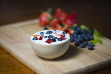 A yogurt cup with strawberries and blueberries placed on a wooden tray.