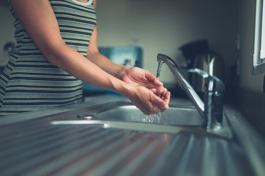Young woman washing her hand in the kitchen sink