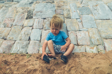 Fototapeta premium Little toddler on beach putting on shoes