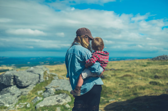 Young mother and toddler admiring view from rock on hill