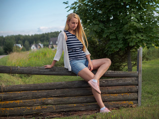 Cute blonde woman posing on old wooden fence in denim shorts