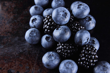 Blueberries and blackberries on a dark background, fresh berries for a vegan, fruits on a rusty background, assorted berry breakfast, copy space