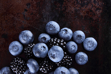 Blueberries and blackberries on a dark background, fresh berries for a vegan, fruits on a rusty background, assorted berry breakfast, copy space