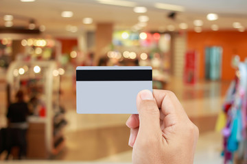 Man hand holding credit card on blur of shopping mall with shining bokeh lights for credit card payment concept