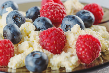Cottage cheese with fresh raspberries and blueberries for a healthy breakfast with ripe berries. Background is a natural healthy product.