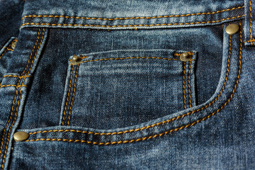 Close-up of a piece of blue jeans with orange stitches. Pocket with rivets close-up.