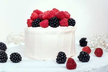 Cake with raspberries and blackberries on white wooden background.