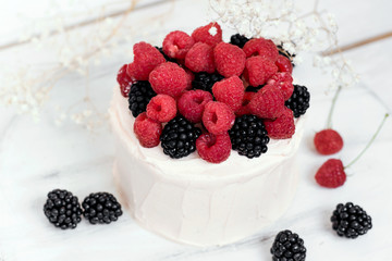 Cake with raspberries and blackberries on white wooden background.